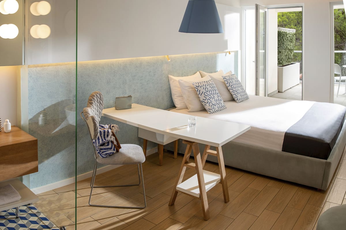 A modern bedroom with a bed, bedside table, chair, and a view of the outdoors.