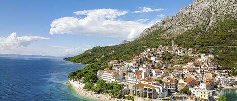 A coastal town with buildings along the shoreline, a clear view of the sea, and a hilly backdrop.