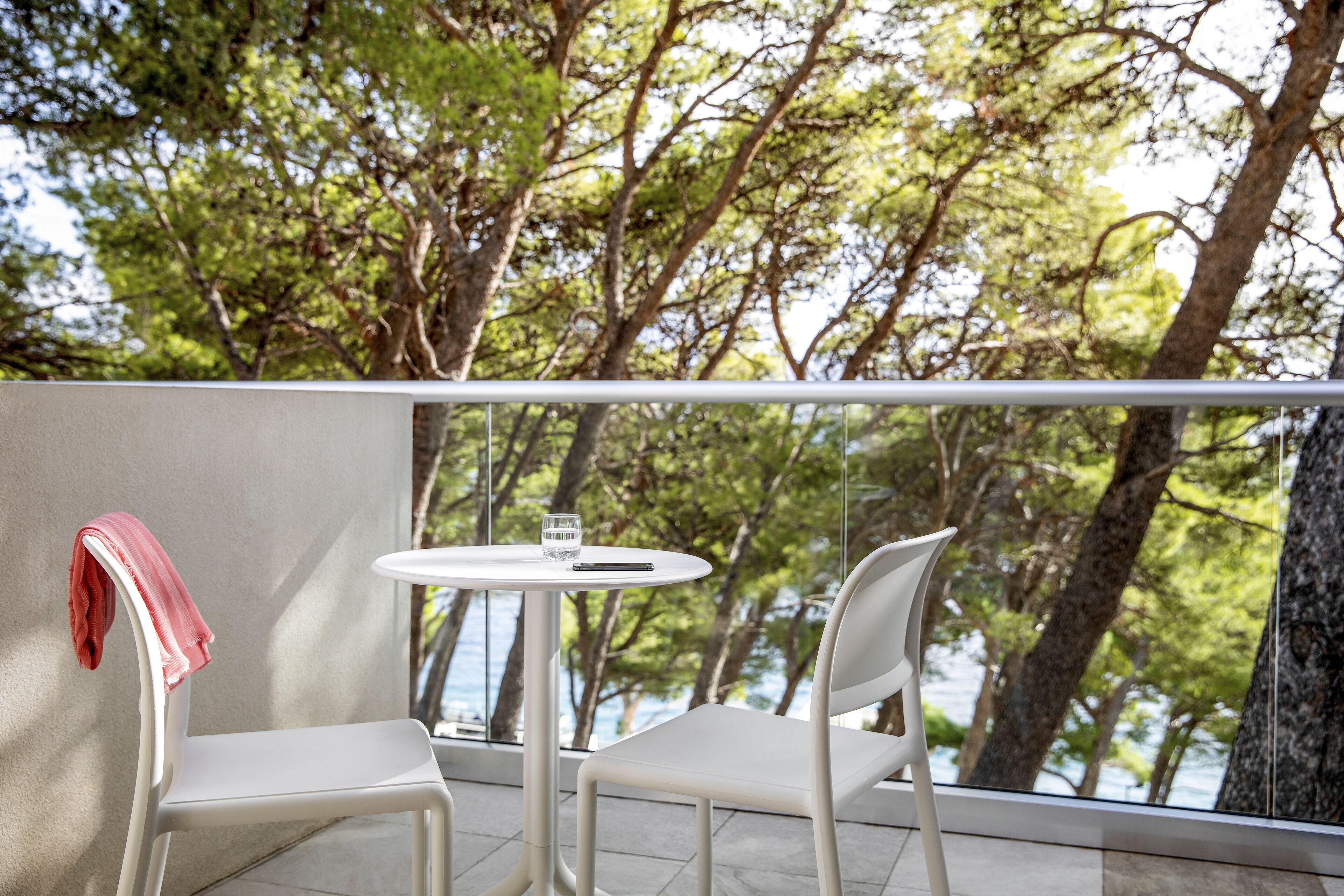 Un balcon avec deux chaises blanches et une petite table ronde, donnant sur une étendue d’eau et des arbres.