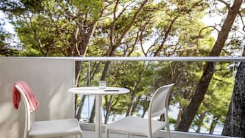A balcony with two white chairs and a small round table, overlooking a body of water and trees.