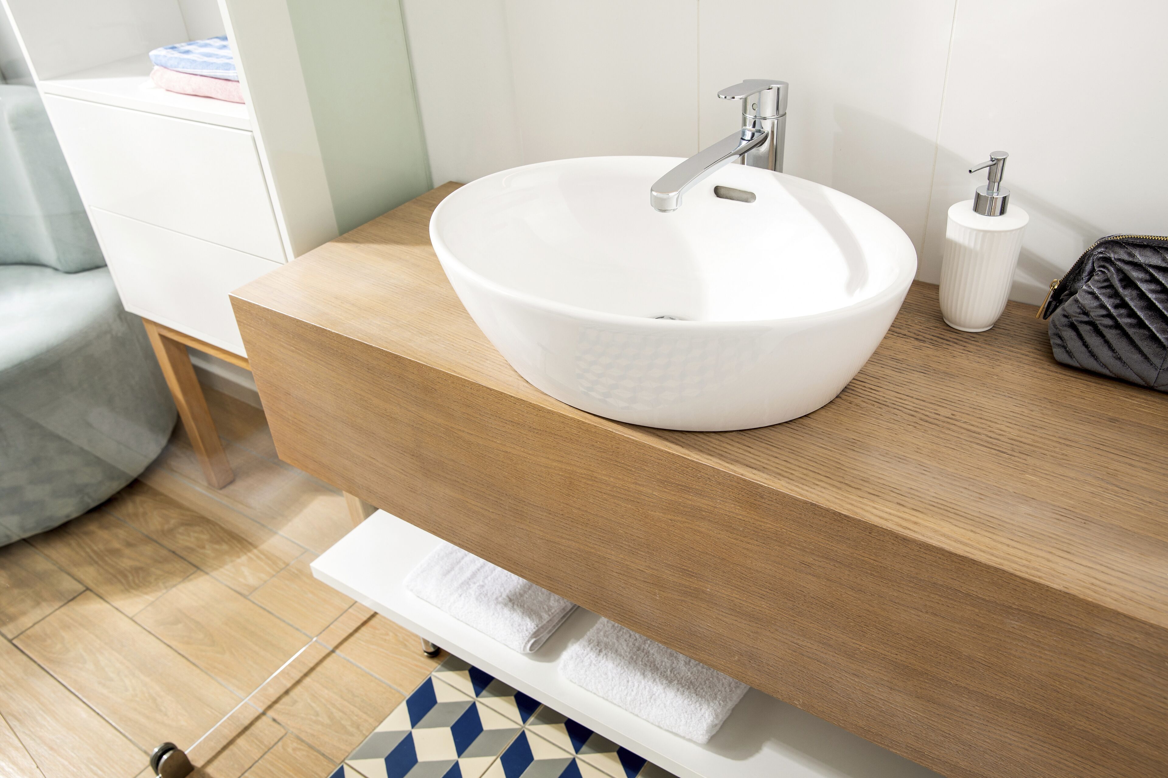 A bathroom with a white vessel sink, wooden countertop, and a towel rack.