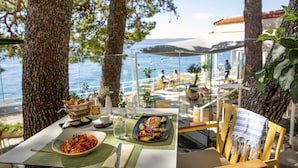 A dining table with a meal, a view of the sea, and outdoor seating.