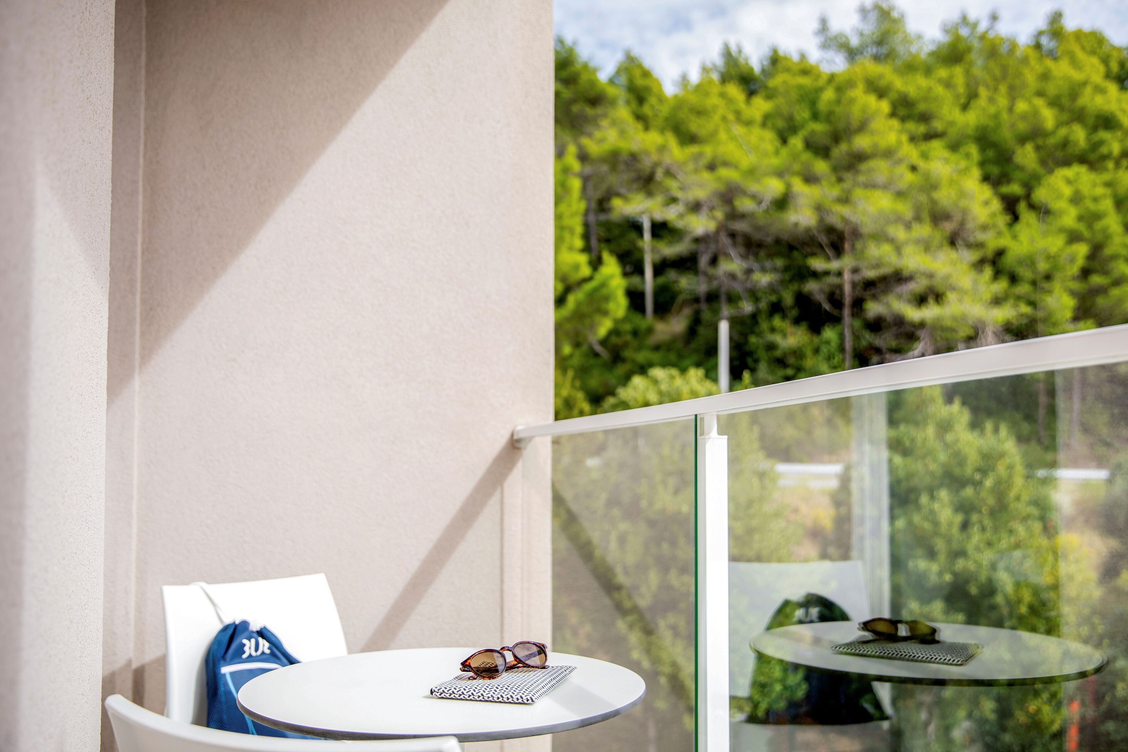 A balcony with a white table and chair, a pair of sunglasses, and a notebook.