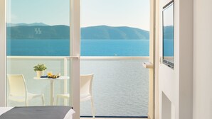 A hotel room with a bed, a round table with fruit and a drink, and a balcony with a view of the sea.