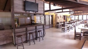 A restaurant with a wooden bar area, multiple seating tables, and a television mounted on the wall. - Hotel JB (Campos do Jordão)