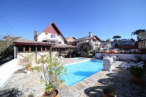 A swimming pool with stone tiles, surrounded by lounge chairs and potted plants. - Hotel JB (Campos do Jordão)