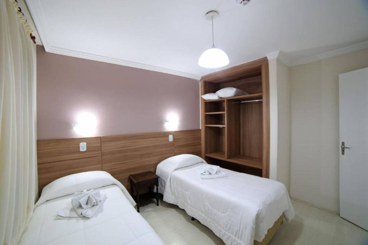 A hotel room with two single beds, a wooden wardrobe, and a small bedside table.