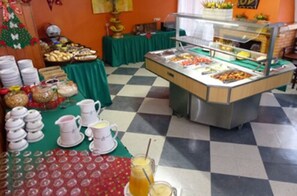 Montaje de bufé con diversos alimentos y bebidas, piso a cuadros y manteles verdes.