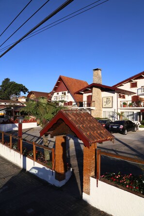 Un hotel con un llamativo letrero 'JBB', un edificio de techo rojo y un estacionamiento con coches.