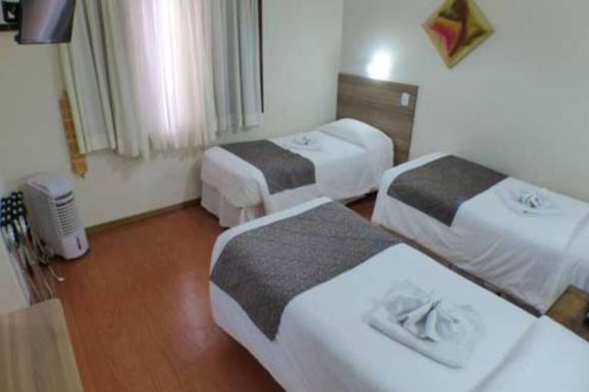 A hotel room with two beds, a TV, a heater, and a window with curtains.
