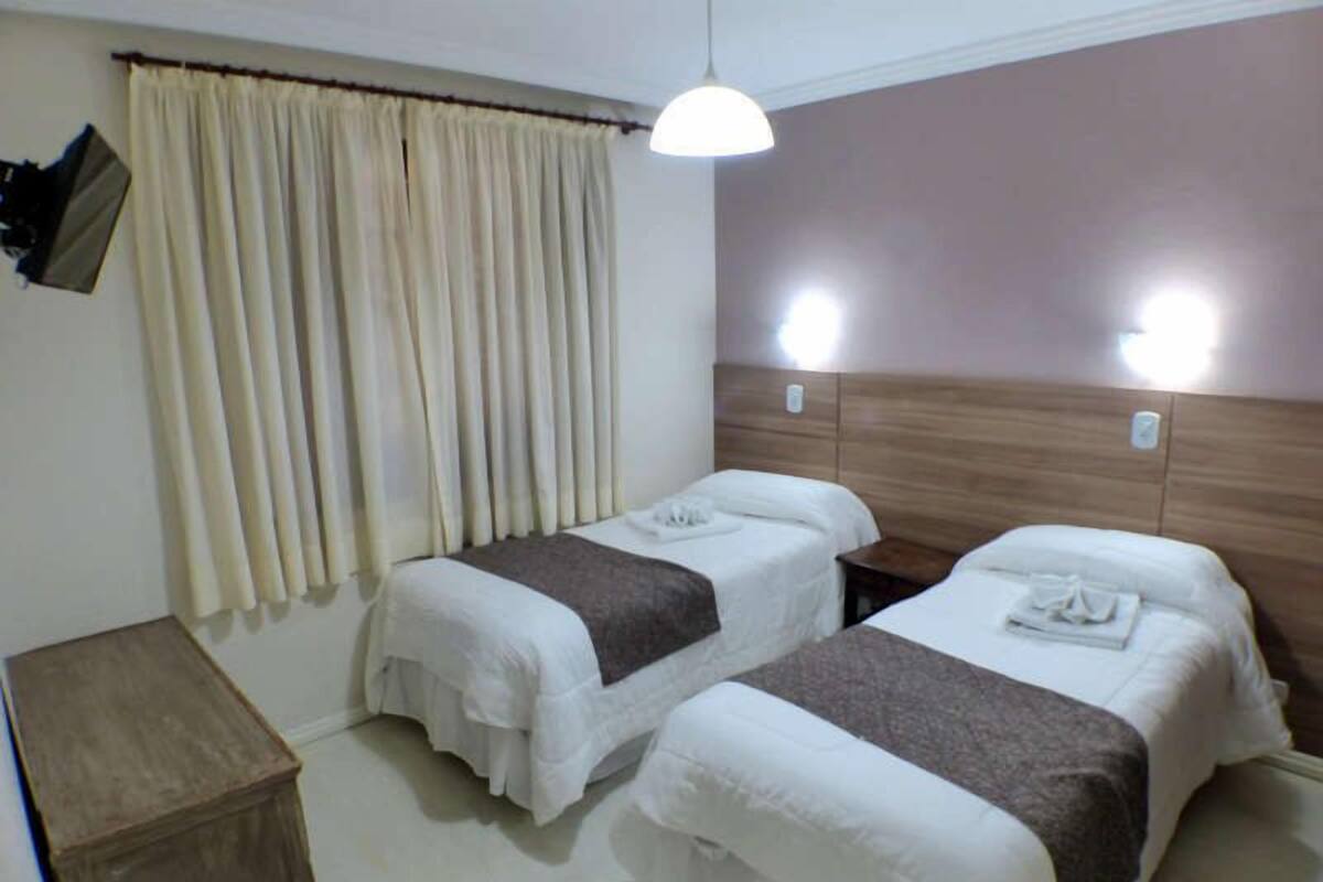 A hotel room with two beds, a wooden headboard, a small wooden table, and a curtain.