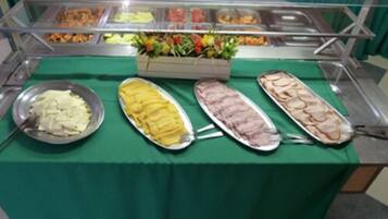 Uma mesa de buffet com diversos alimentos, incluindo uma salada, um prato amarelo e um prato com carne.