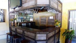 A bar area with stools, a counter, and a shelf of bottles. - Hotel JB (Campos do Jordão)