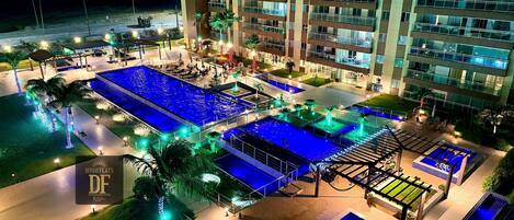 A hotel with multiple swimming pools, outdoor seating areas, and a large building with balconies.