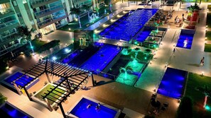A rooftop pool area with multiple pools, palm trees, and a building in the background. - Vg Fun by Diego Flats (Fortaleza)