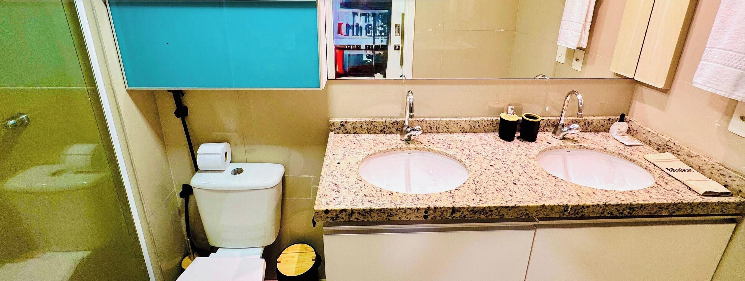 A bathroom with a toilet, two sinks, and a mirror.