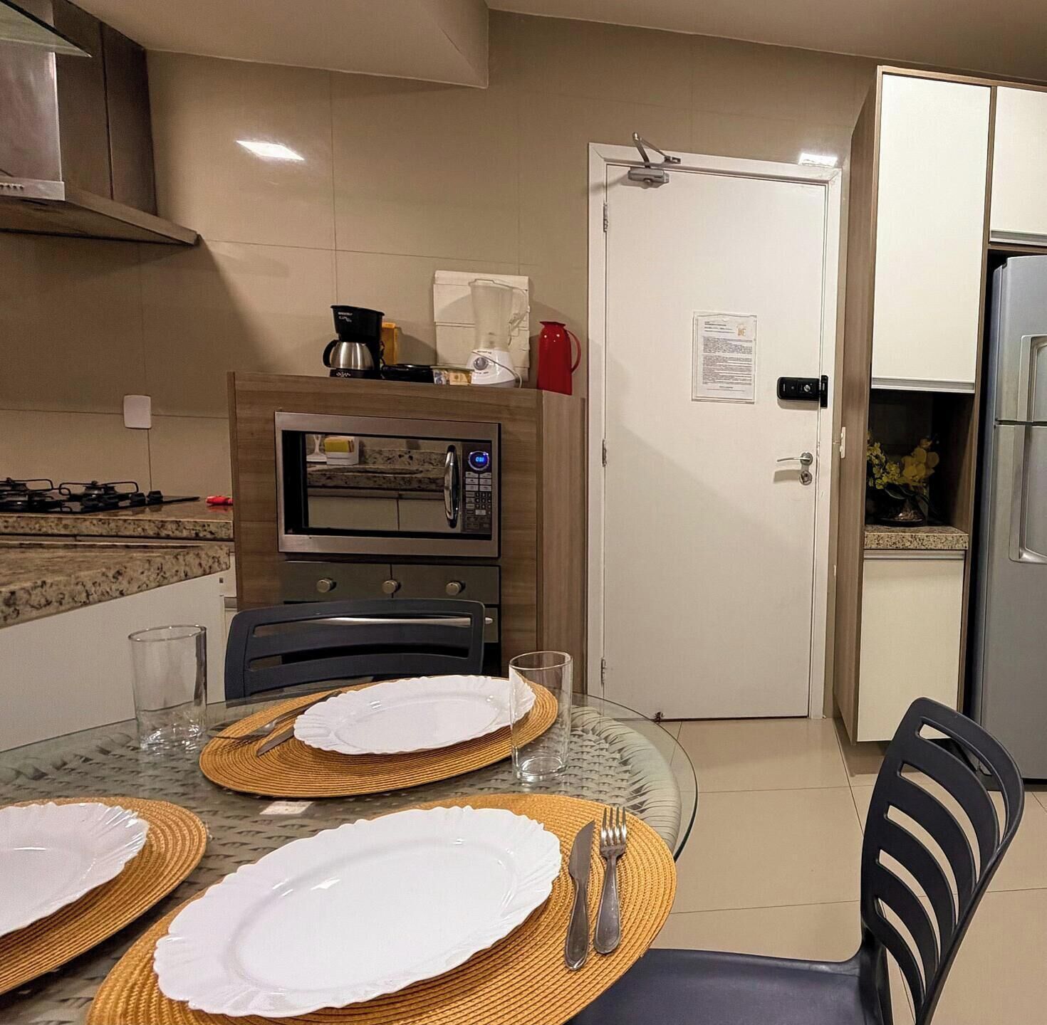 A modern kitchen with a microwave, stove, and refrigerator. There is a dining table set with plates and cutlery.