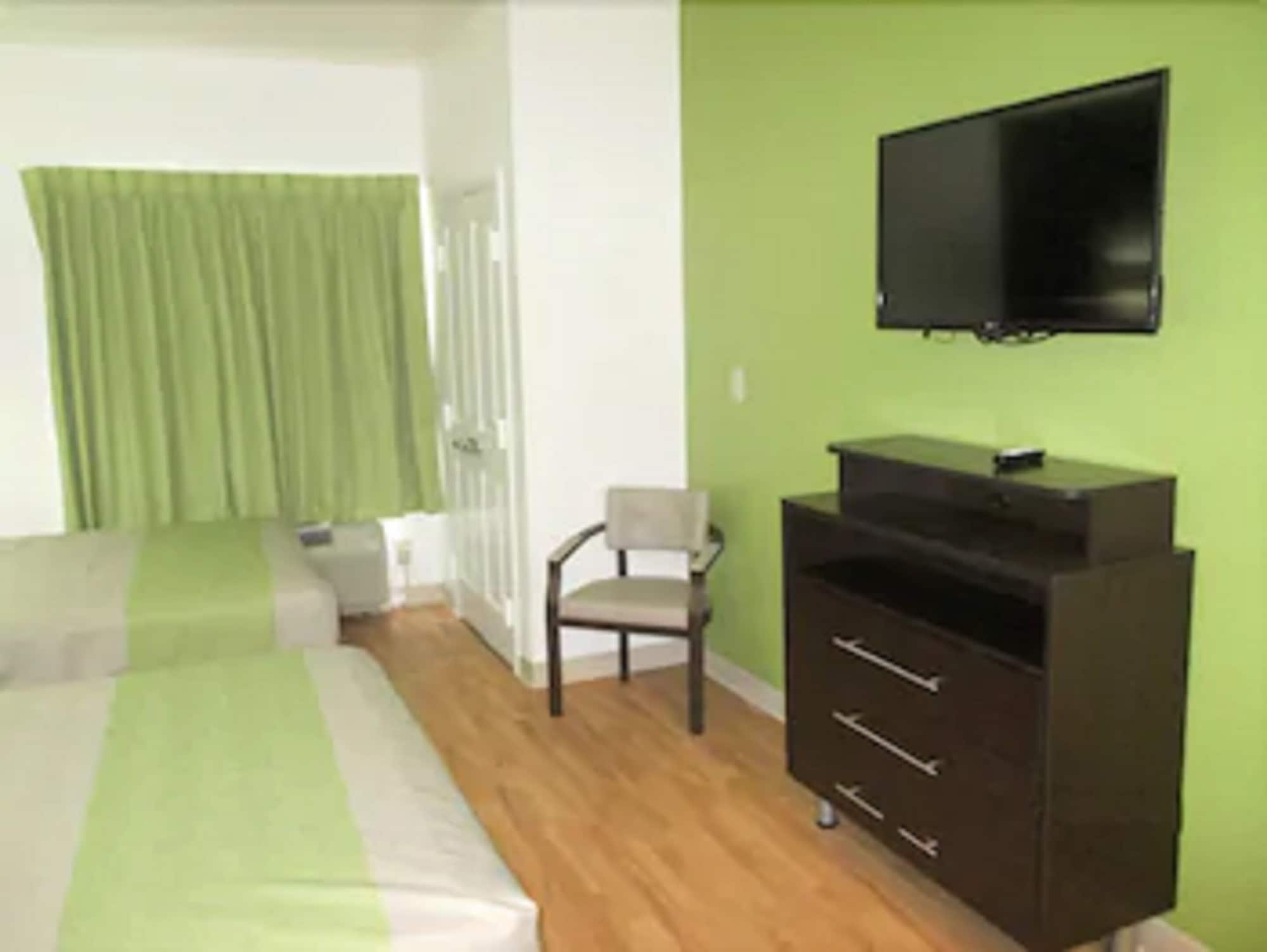 A room with a bed, a chair, a TV, and a dresser.