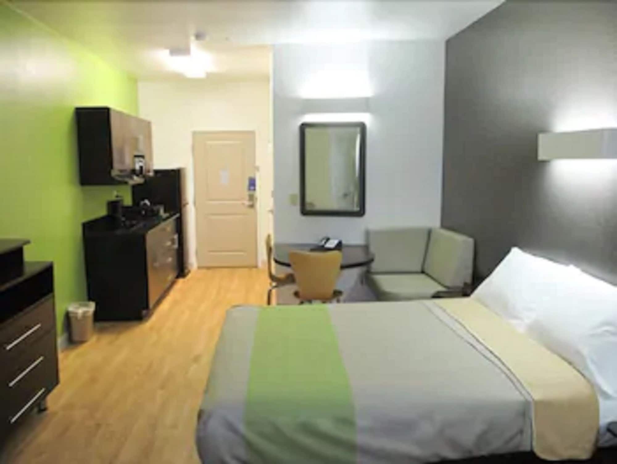 A hotel room with a bed, a desk, a chair, a wardrobe, and a kitchenette.