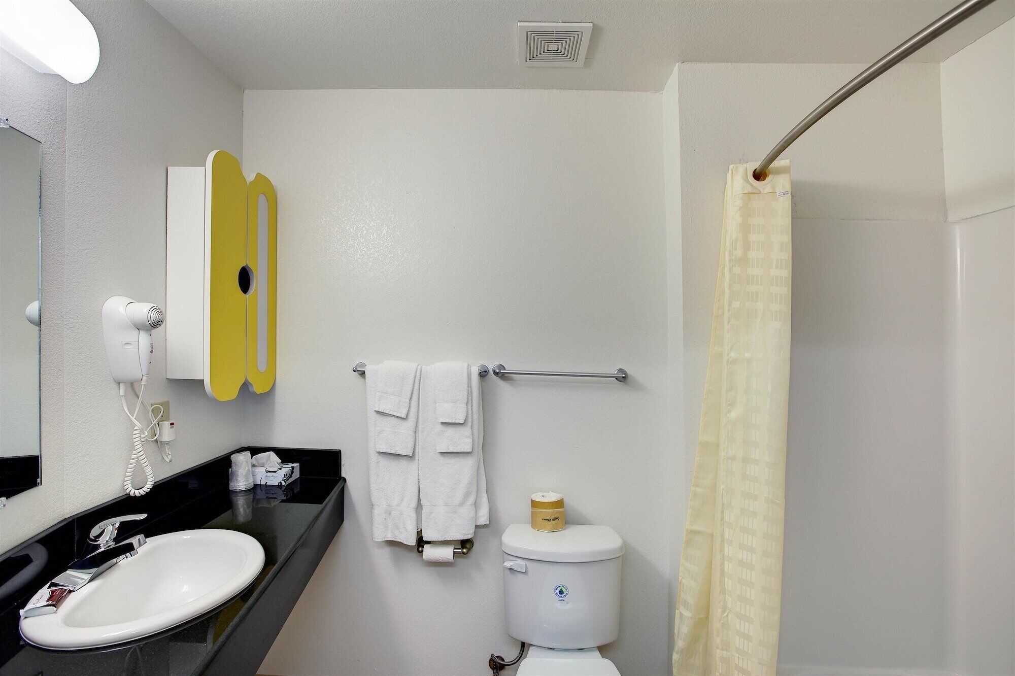 A bathroom with a white sink, a yellow towel rack, a white toilet, and a shower curtain.