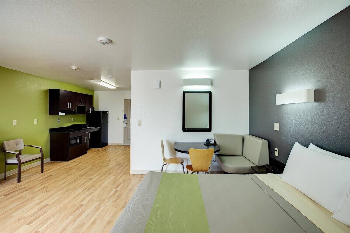 A hotel room with a bed, a desk, a chair, a sofa, and a kitchenette.
