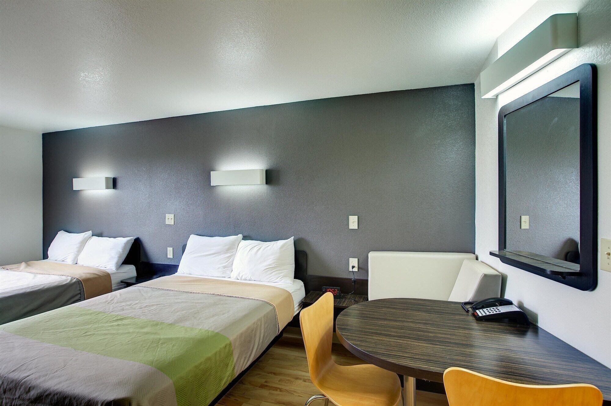 A hotel room with two beds, a desk with a chair, a TV, and a clock on the wall.