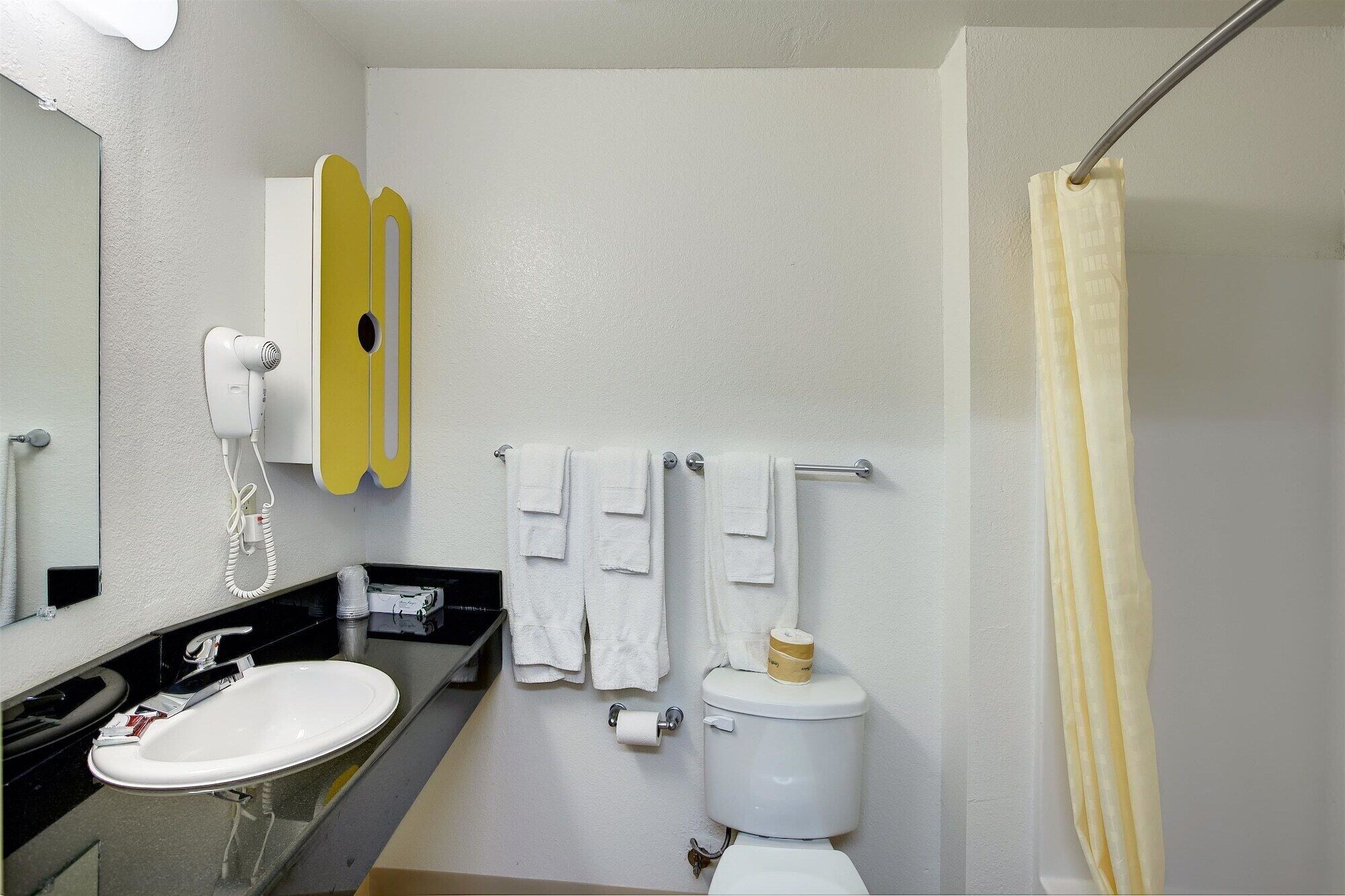 A bathroom with a white sink, a toilet, a shower curtain, and a towel rack with towels.