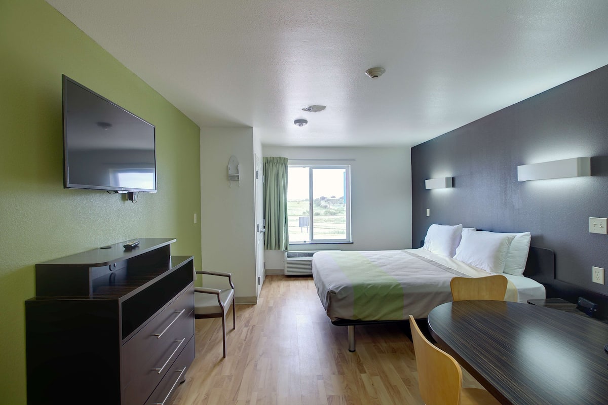 A hotel room with a bed, a desk, a dresser, a TV, and a window with curtains.