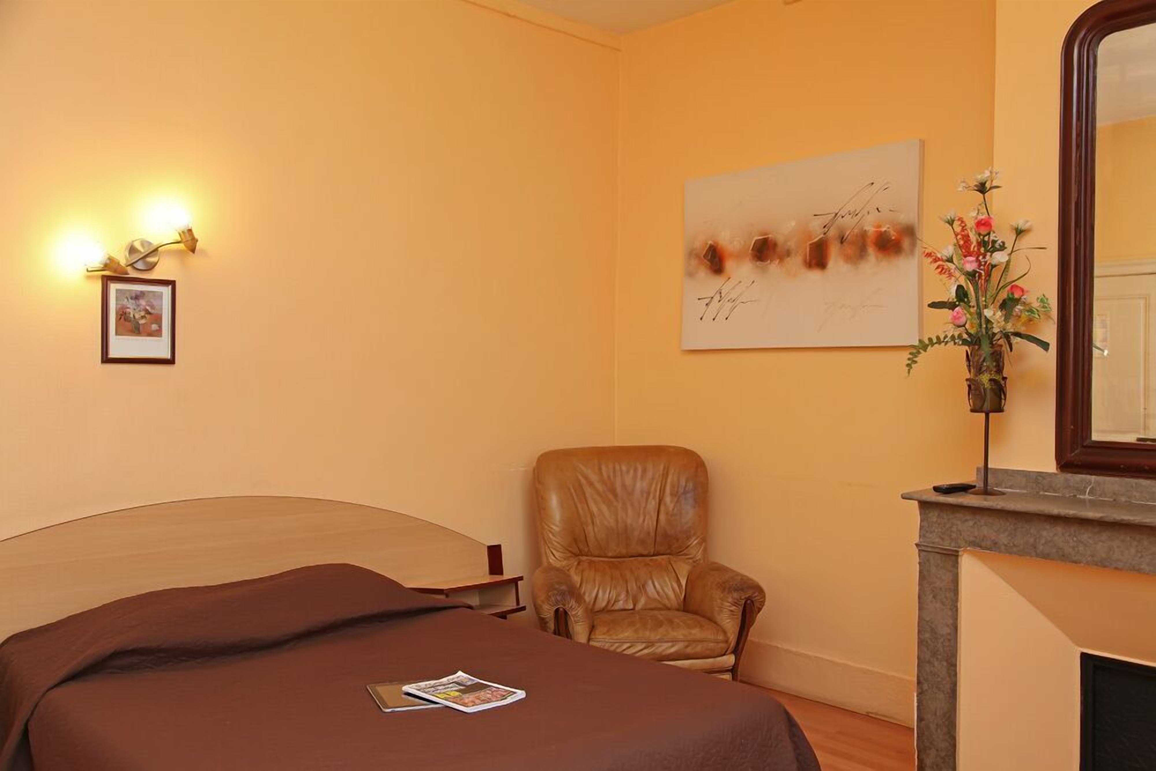 Une chambre d’hôtel comprenant un lit, un fauteuil en cuir, une cheminée et une œuvre d’art accrochée au mur.