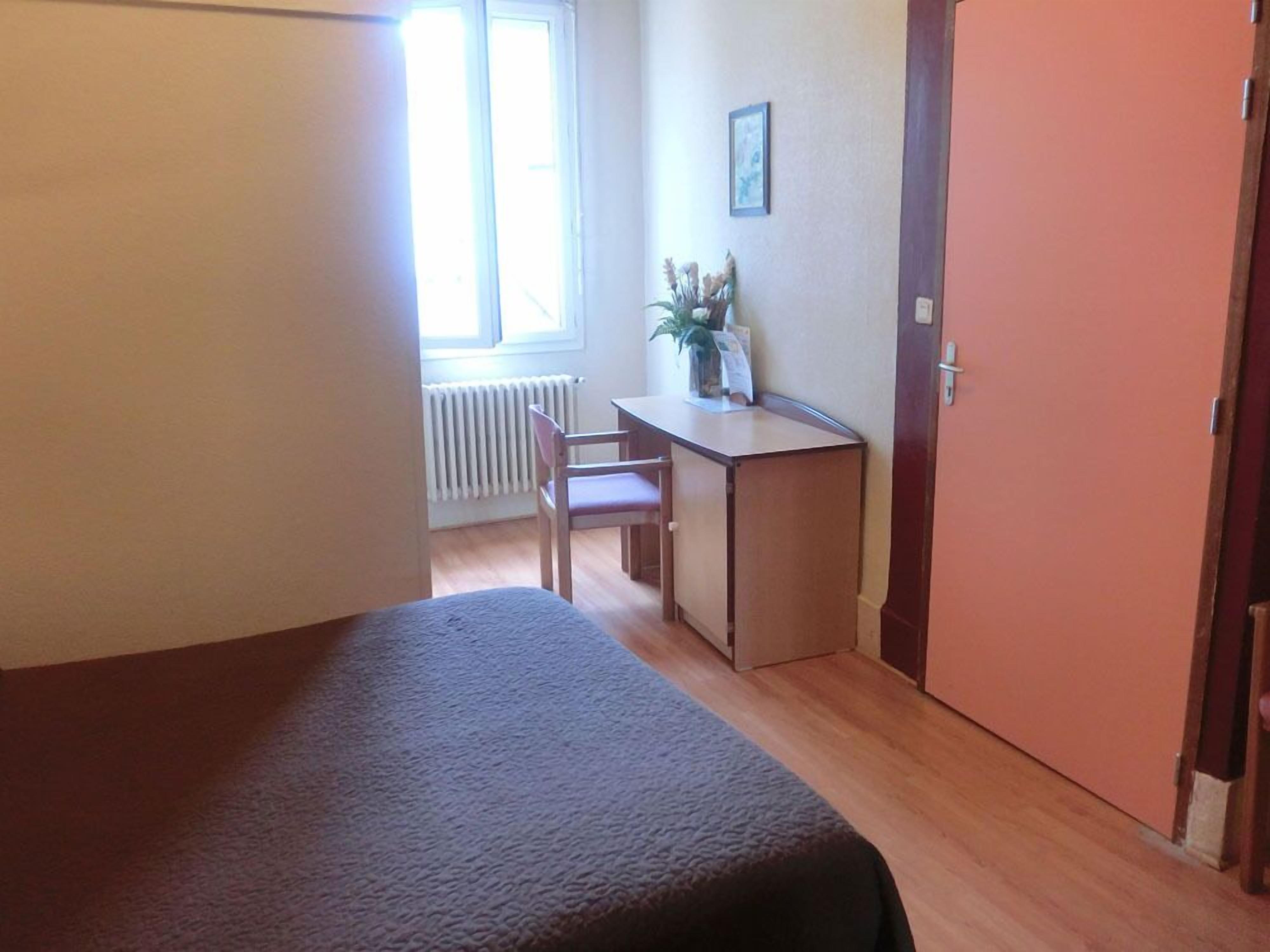 Une petite pièce comprenant un lit, un bureau, une chaise et un radiateur.