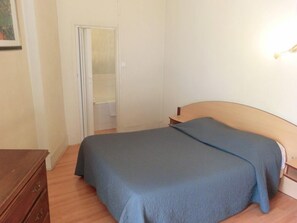 A bedroom with a bed, a wooden dresser, and a door leading to a bathroom. - Hotel Le Terminus d'Albi (Albi)
