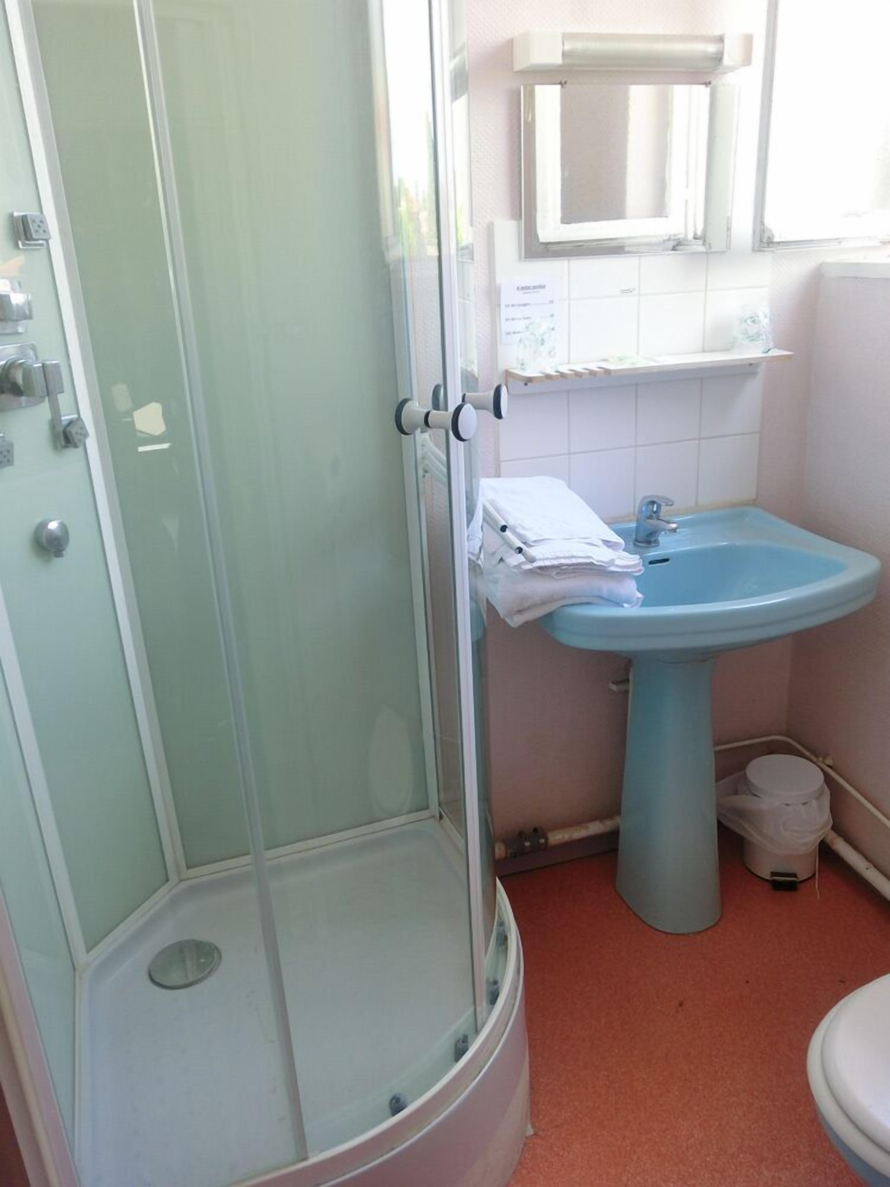 Une salle de bain avec une douche à parois de verre, un lavabo sur colonne et des toilettes.