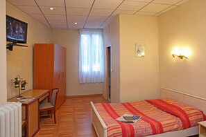 A hotel room with a bed, a desk, a chair, a television, and a window with curtains. - Hotel Le Terminus d'Albi (Albi)