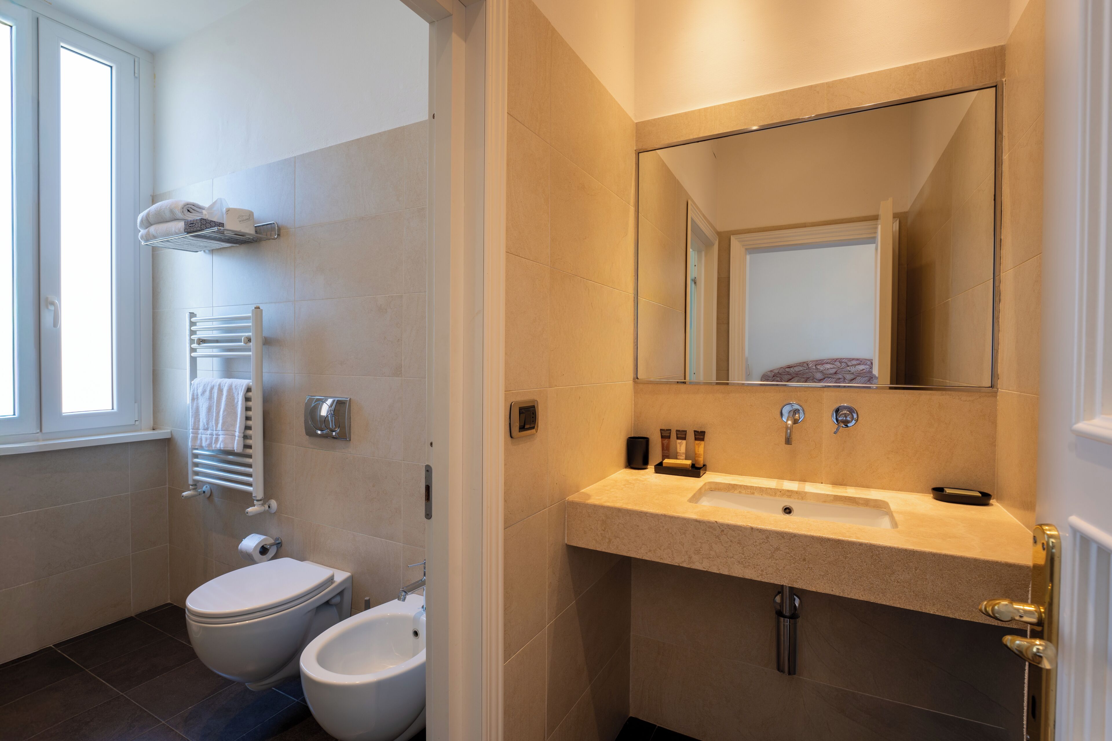 Une salle de bain moderne équipée de toilettes, d’un bidet, d’un porte-serviettes et d’un lavabo avec un miroir au-dessus.