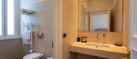 Une salle de bain moderne équipée de toilettes, d’un bidet, d’un porte-serviettes et d’un lavabo avec un miroir au-dessus.