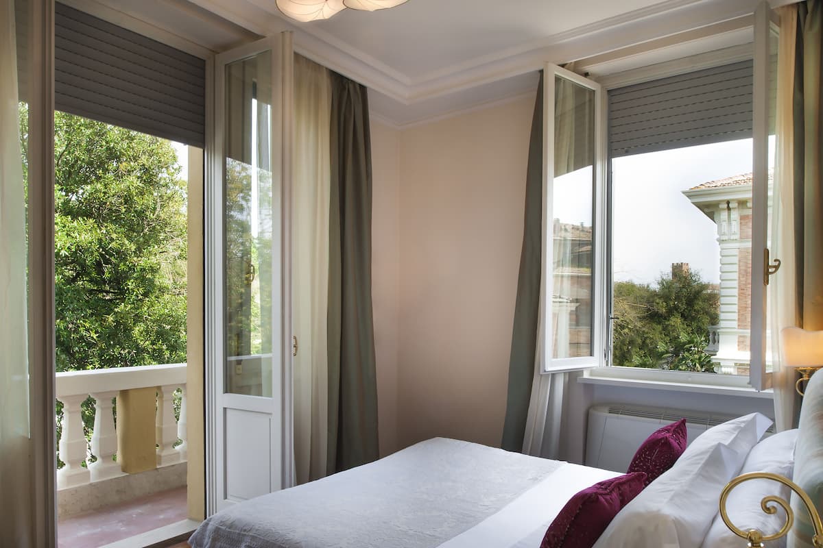 A hotel room with a bed, a window with curtains, and a view of greenery outside.