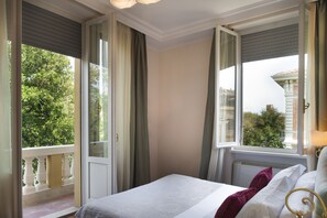 A hotel room with a bed, a window with curtains, and a view of greenery outside.