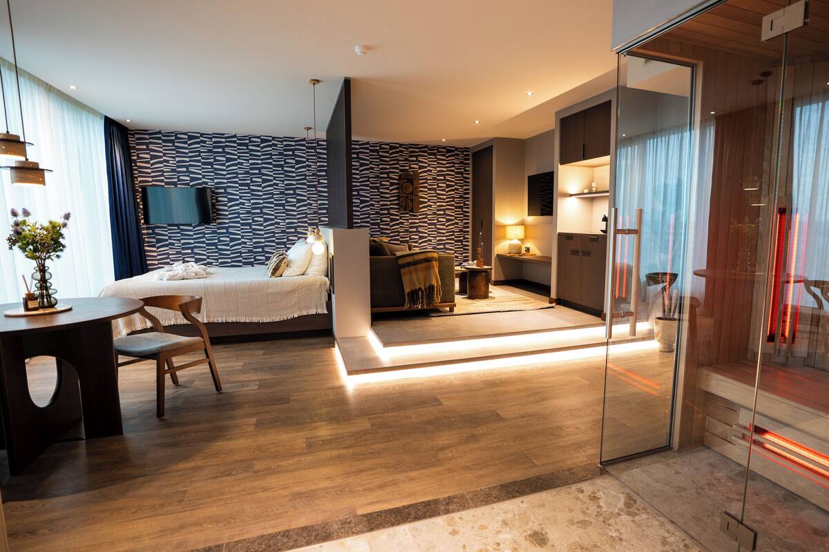 A modern hotel room with a bed, seating area, and a glass partition.