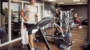 Een sportschool met loopbanden, trainingsapparaten en een persoon die op een loopband aan het rennen is.