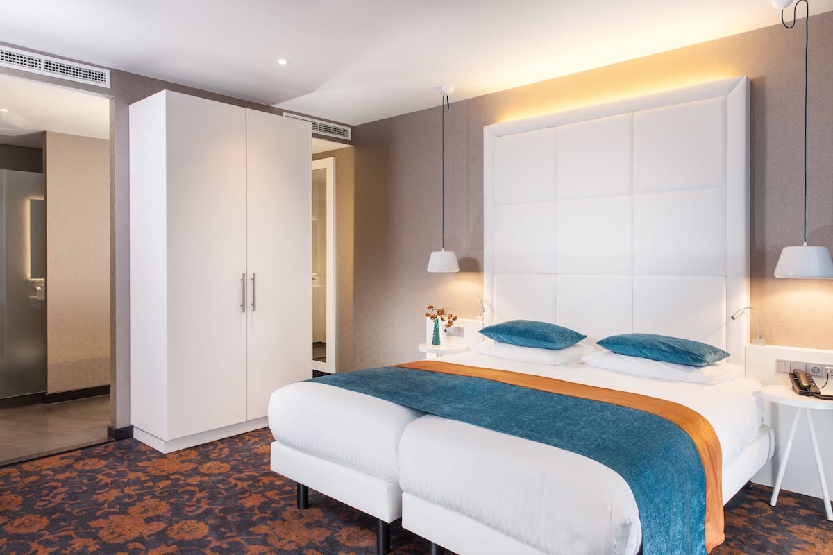A hotel room with a large bed, a wardrobe, a bedside table with a lamp, and a small table with a vase of flowers.