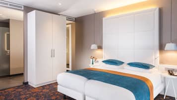 Hotelkamer met een groot bed, een kledingkast, een nachtkastje met lamp en een tafeltje met een bloemenvaas.