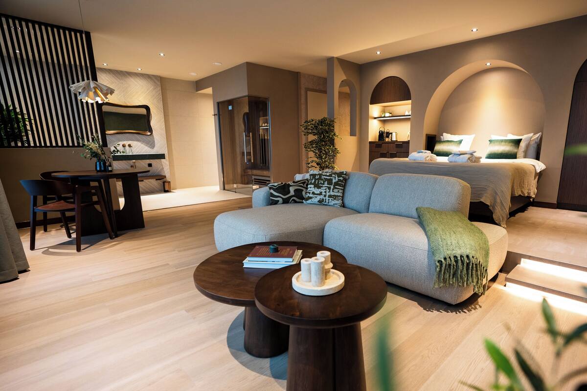 A modern hotel room with a sofa, a dining table, and a bed with a headboard.