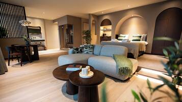 A modern hotel room with a sofa, a dining table, and a bed with a headboard.