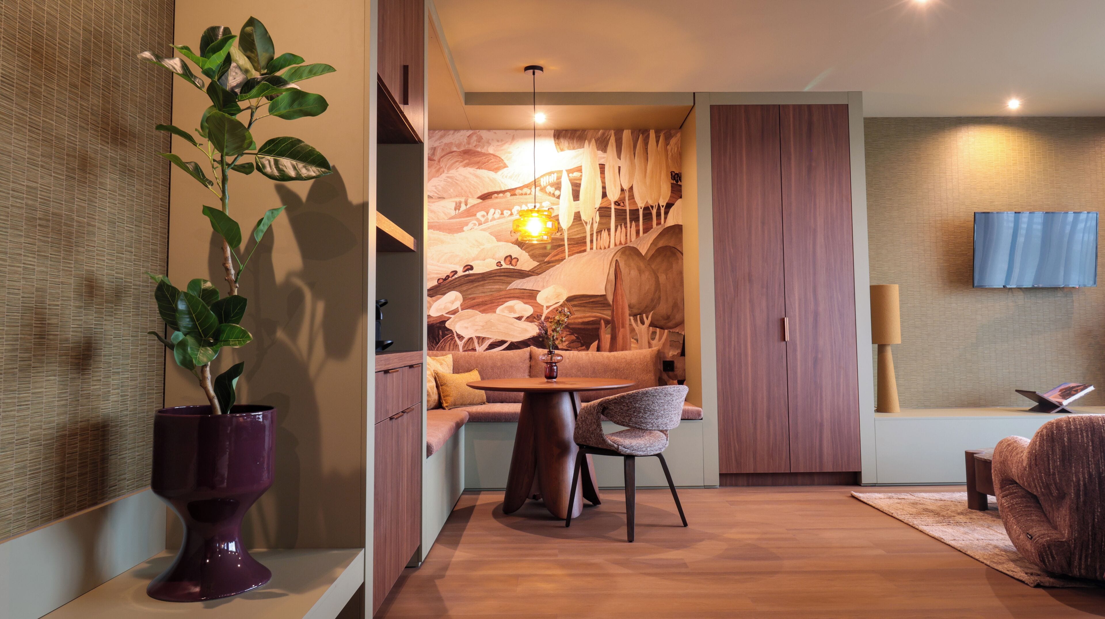 Una sala de estar moderna con comedor, una planta grande en maceta, un sofá, una mesa de centro y un televisor montado en la pared.
