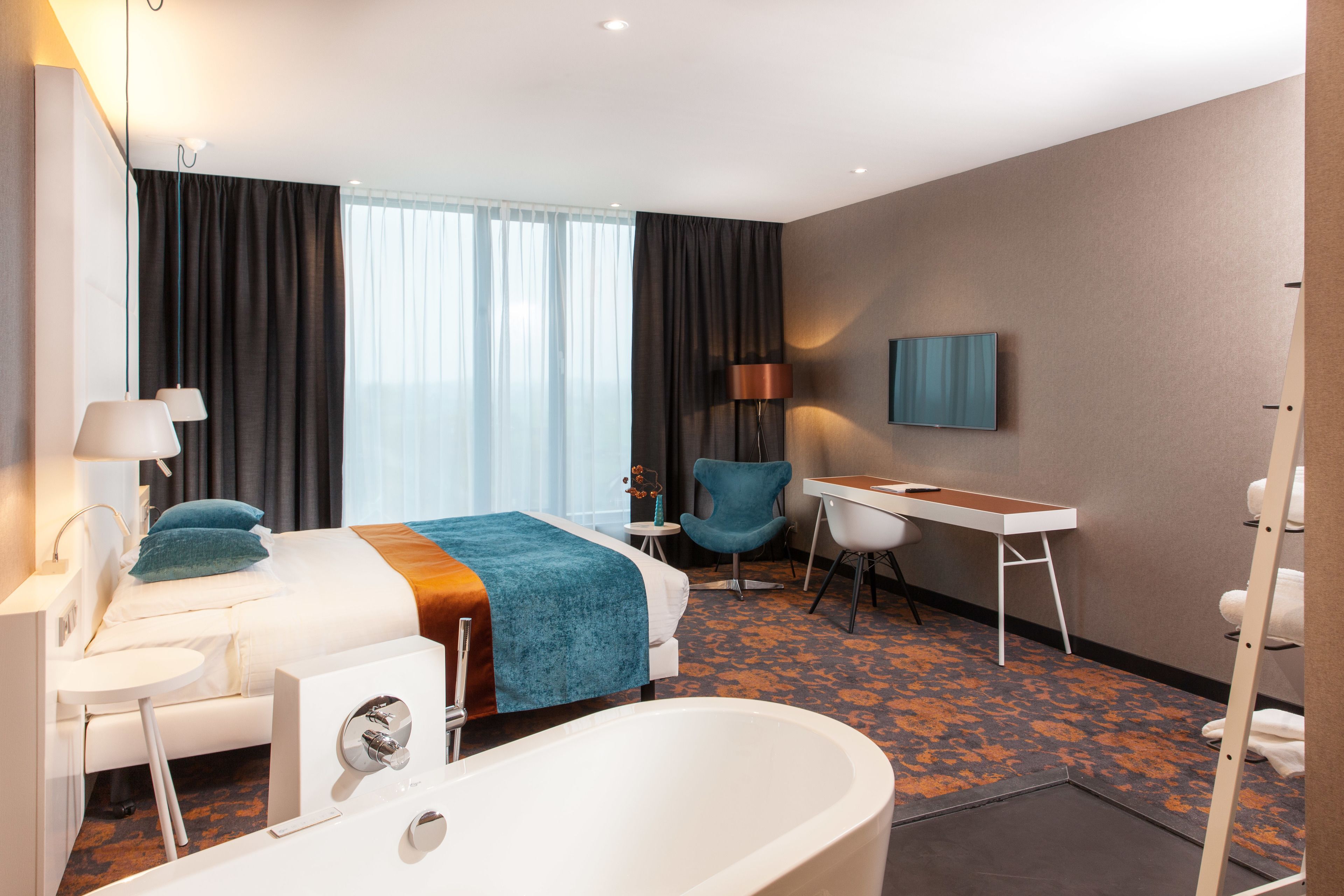 Une chambre d’hôtel équipée d’un lit, d’un bureau, d’une chaise, d’une baignoire et d’un téléviseur.