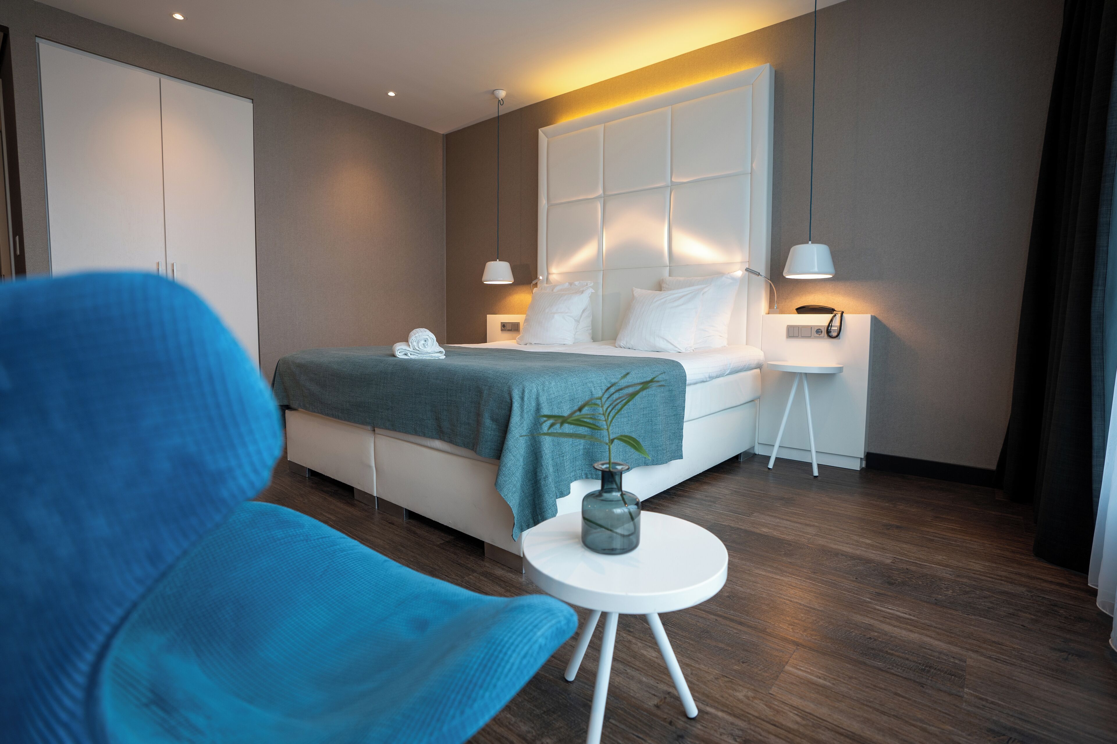A modern bedroom with a bed, bedside tables, a chair, and a small table with a vase.