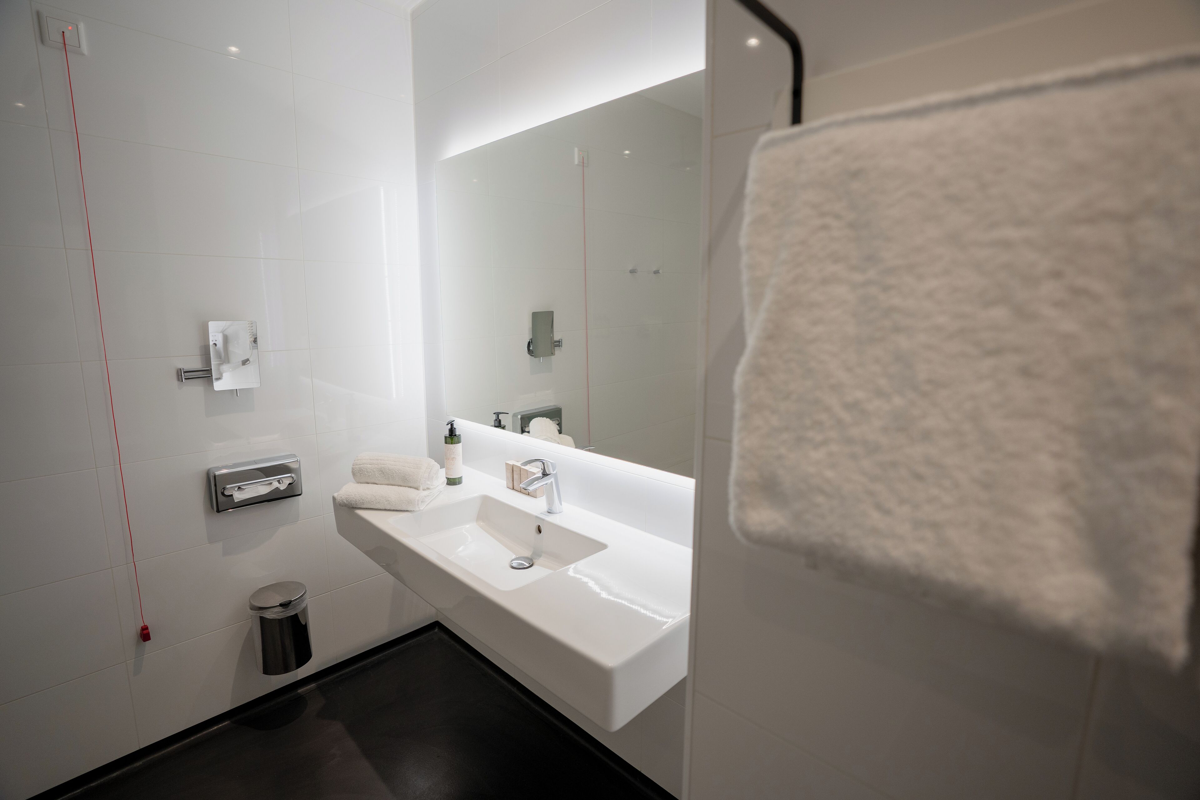 A modern bathroom with a white sink, mirror, and towel rack.