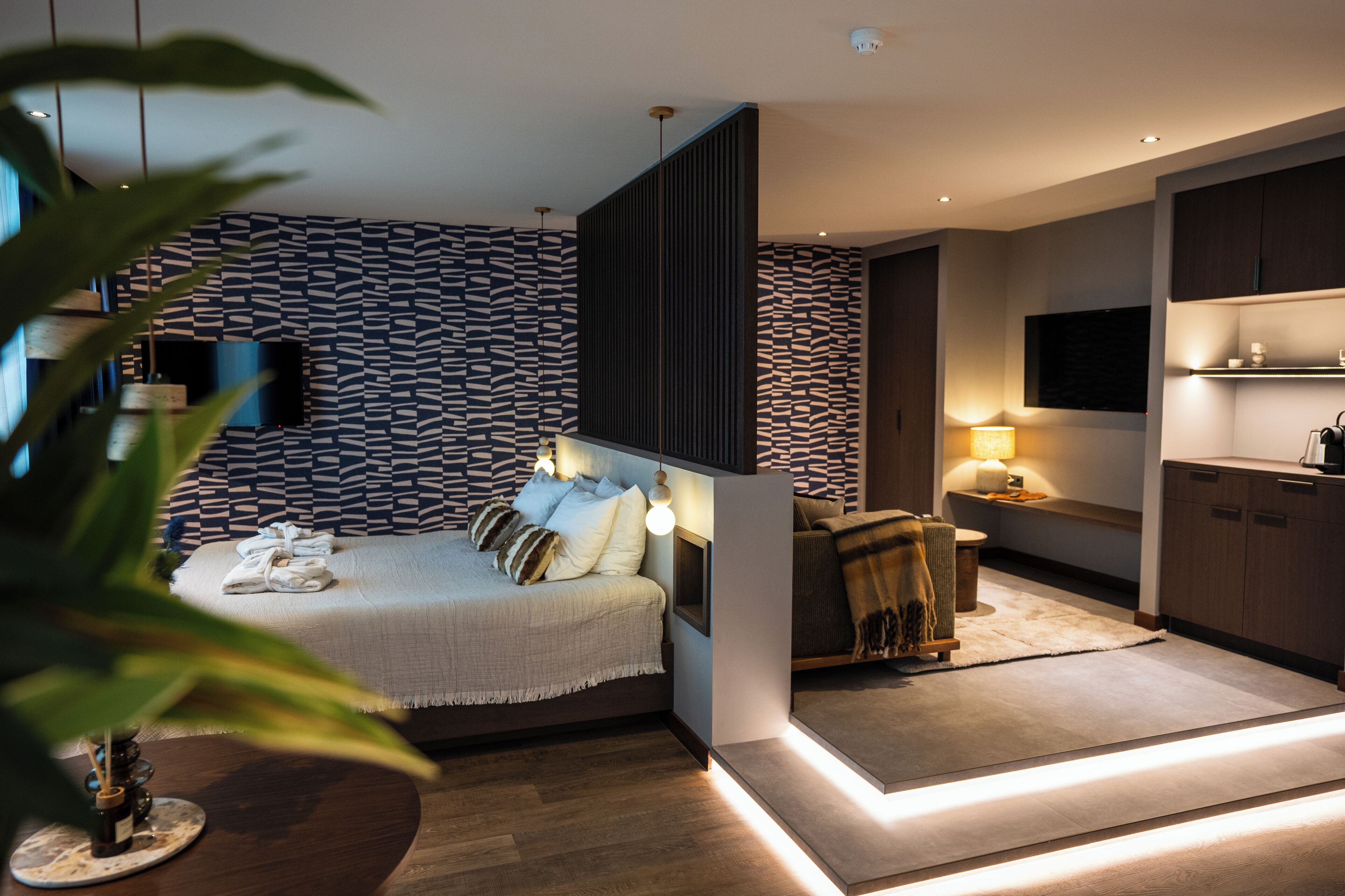 Een moderne slaapkamer met een bed, nachtkastje en een aan de muur bevestigde televisie.