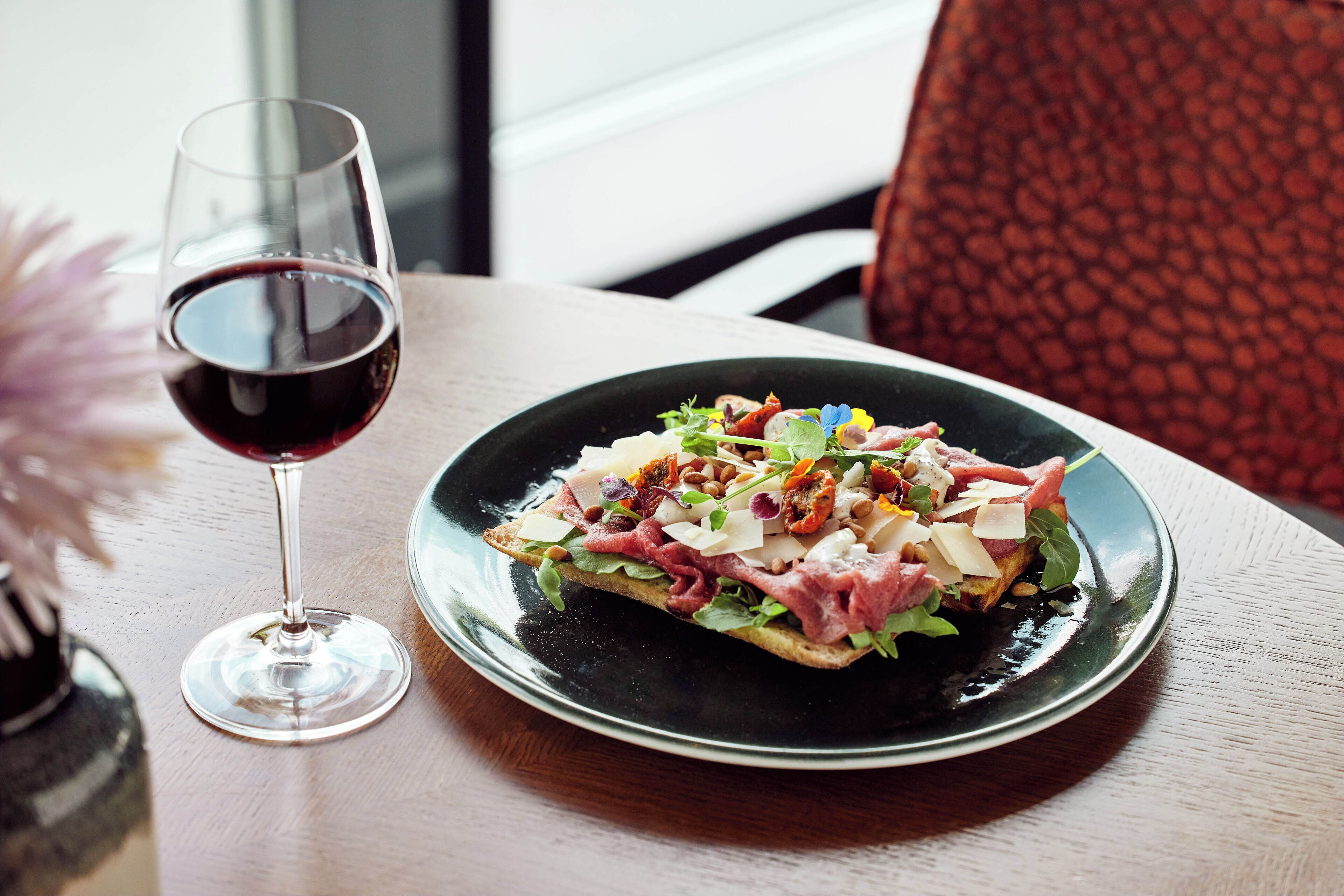 A plate of food with a glass of red wine on a table.