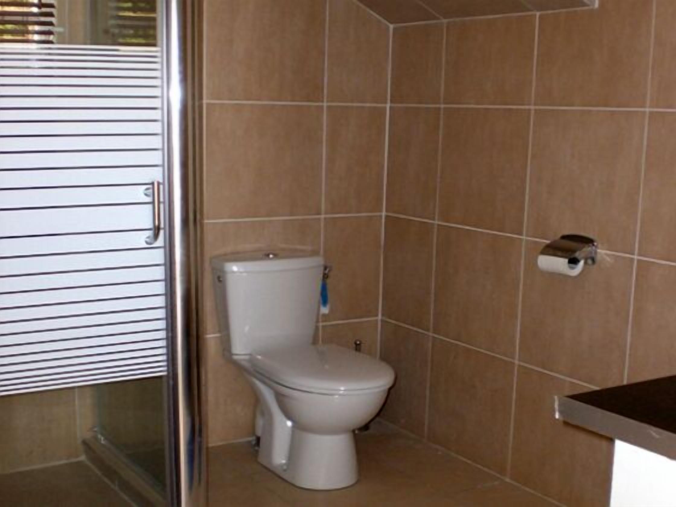 A bathroom with a toilet, a shower area, and a tiled wall.